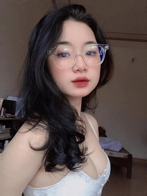 Cô gái tóc dài đeo kính, tạo dáng bên cửa sổ.